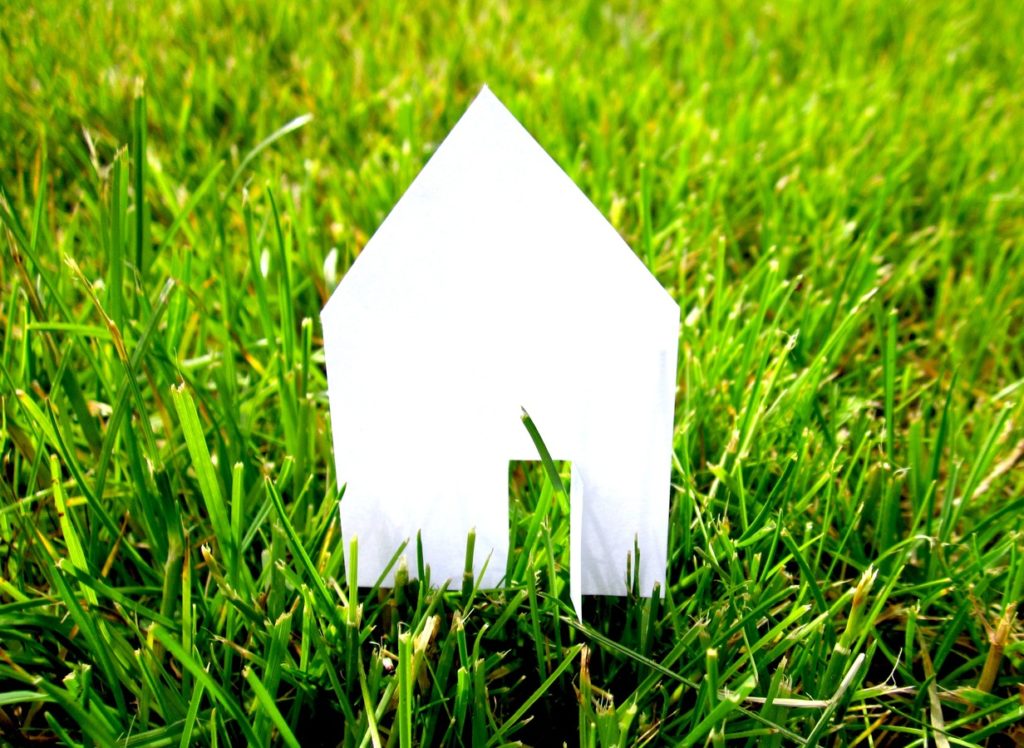 maison blanche en papier sur pelouse verte symbolisant l'investissement immobilier