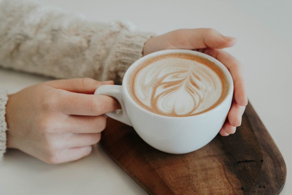 mains tenant une tasse de café avec latte art en forme de feuille