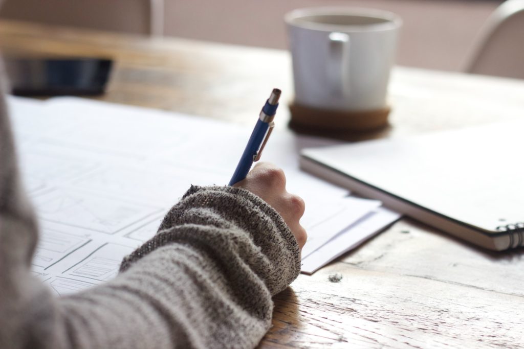 personne écrivant avec un stylo sur des documents de travail à côté d'une tasse de café