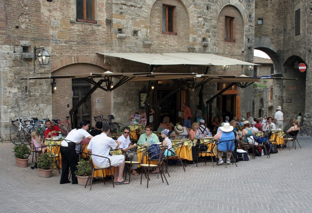 terrasse de restaurant italien en pierre avec chaises jaunes et parasol blanc