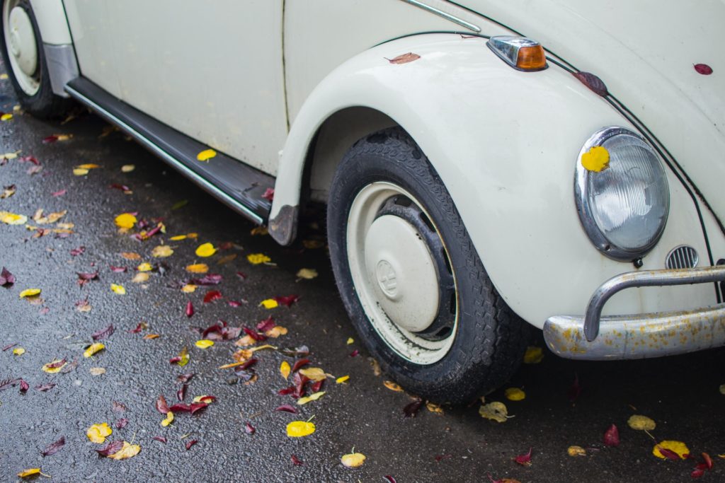 pneus d'une petite voiture blanche garée sur route mouillée avec feuilles d'automne