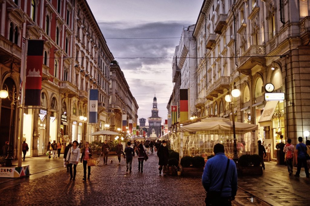 rue piétonne illuminée avec galeries marchandes et tour médiévale en arrière-plan, milan italie