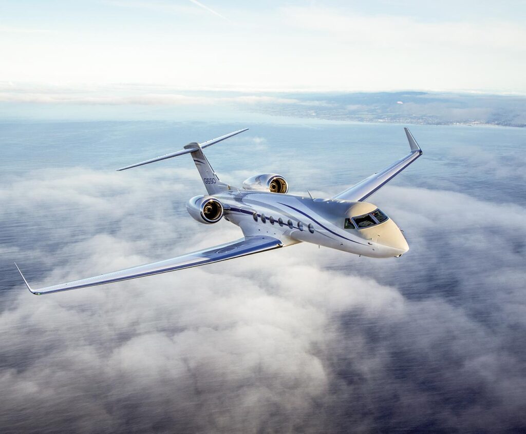 jet privé blanc et bleu volant au-dessus des nuages avec mer et côte en arrière-plan
