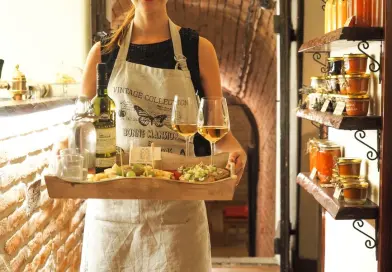 A waitress in a vintage apron serves wine and appetizers in a cozy, rustic indoor setting.