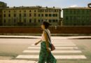 Comment s’habiller en Italie femme : guide complet par saison Casual stroll in historic Pisa, Tuscany with a side view of a woman crossing a sunlit street near old buildings.