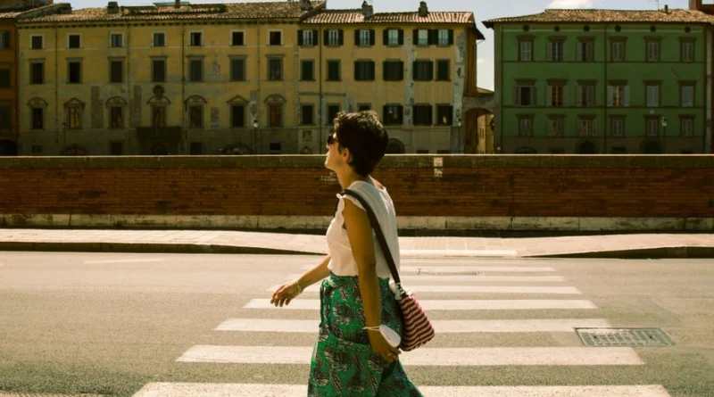 Casual stroll in historic Pisa, Tuscany with a side view of a woman crossing a sunlit street near old buildings.