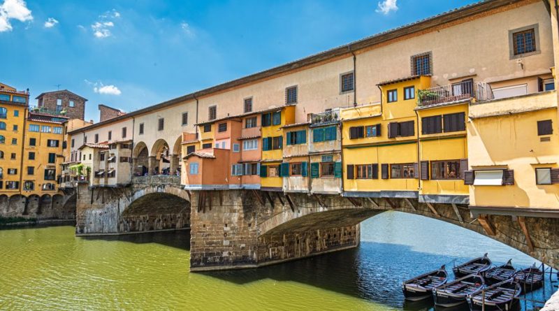 Sunny view of Ponte Vecchio, a historic bridge with colorful shops over the Arno River in Florence, Italy.