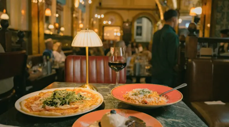A pizza, pasta, and dessert on a marble table in a dimly lit restaurant