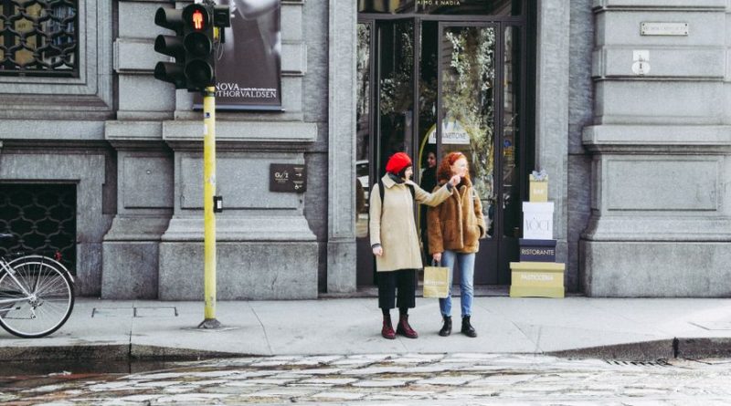 Two women stand by a streetlight in Milan, Italy, near a fashion store.