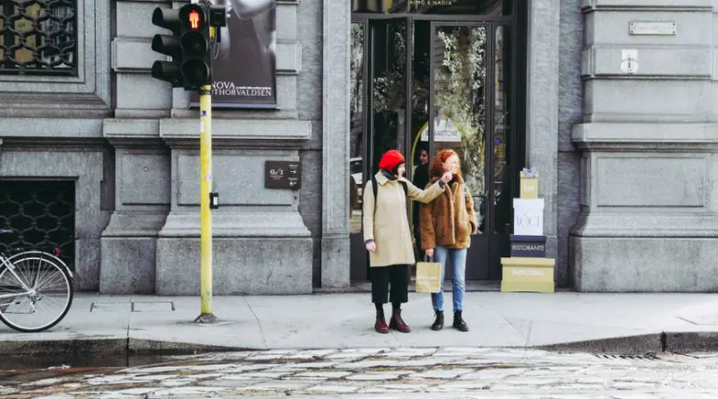 Two women stand by a streetlight in Milan, Italy, near a fashion store.