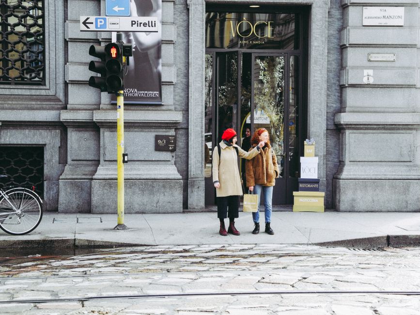 Two women stand by a streetlight in Milan, Italy, near a fashion store.