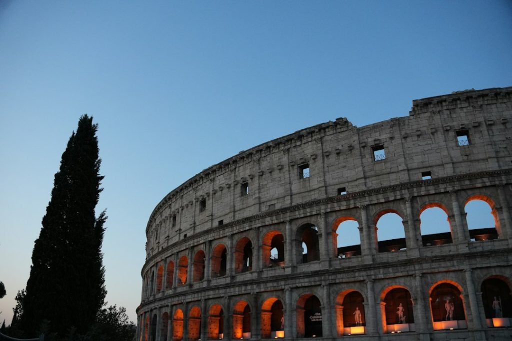 The colosseum illuminated at dusk with a tall tree