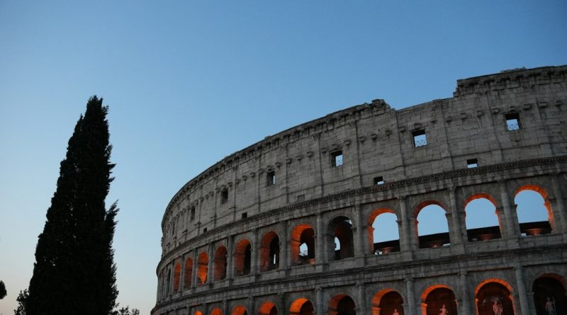 The colosseum illuminated at dusk with a tall tree